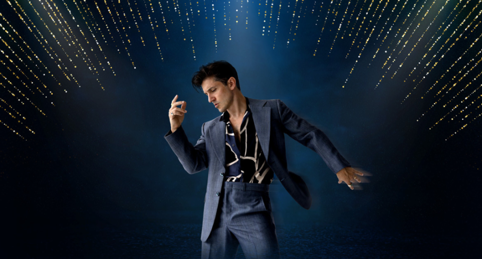 A man dressed in a dark suit poses like Elvis