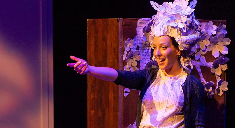 A performer smiles and points in a large paper headdress