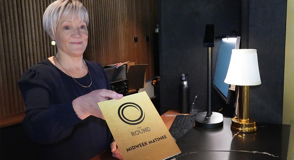 A woman hands out a brochure in the box office at The Round