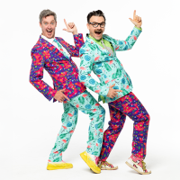 Two men in brightly coloured suits point their index fingers in the air and smile. 