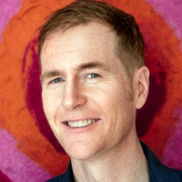 A man smiles at the camera, with pink and red circles behind him.