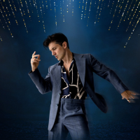 A man dressed in a dark suit poses like Elvis