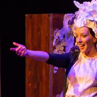 A performer smiles and points in a large paper headdress