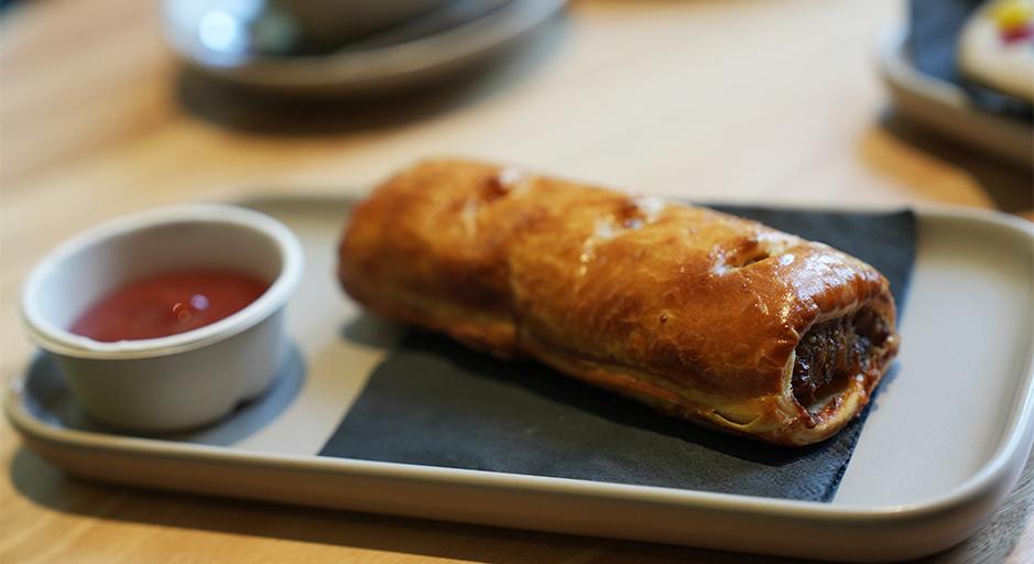 Sausage roll on a plate and sauce in a container